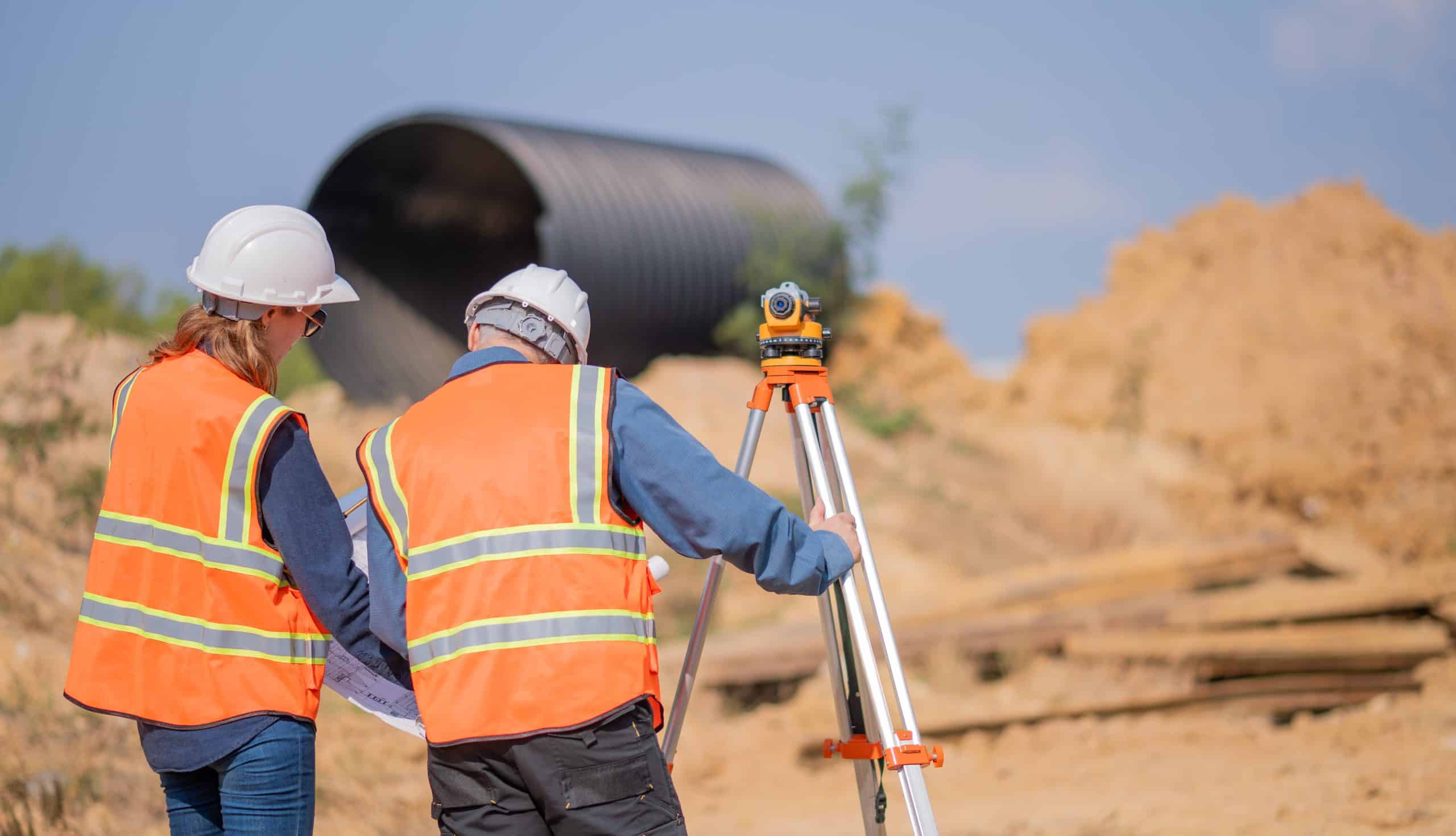 a group of men in safety vests and helmets standing next to a tripod