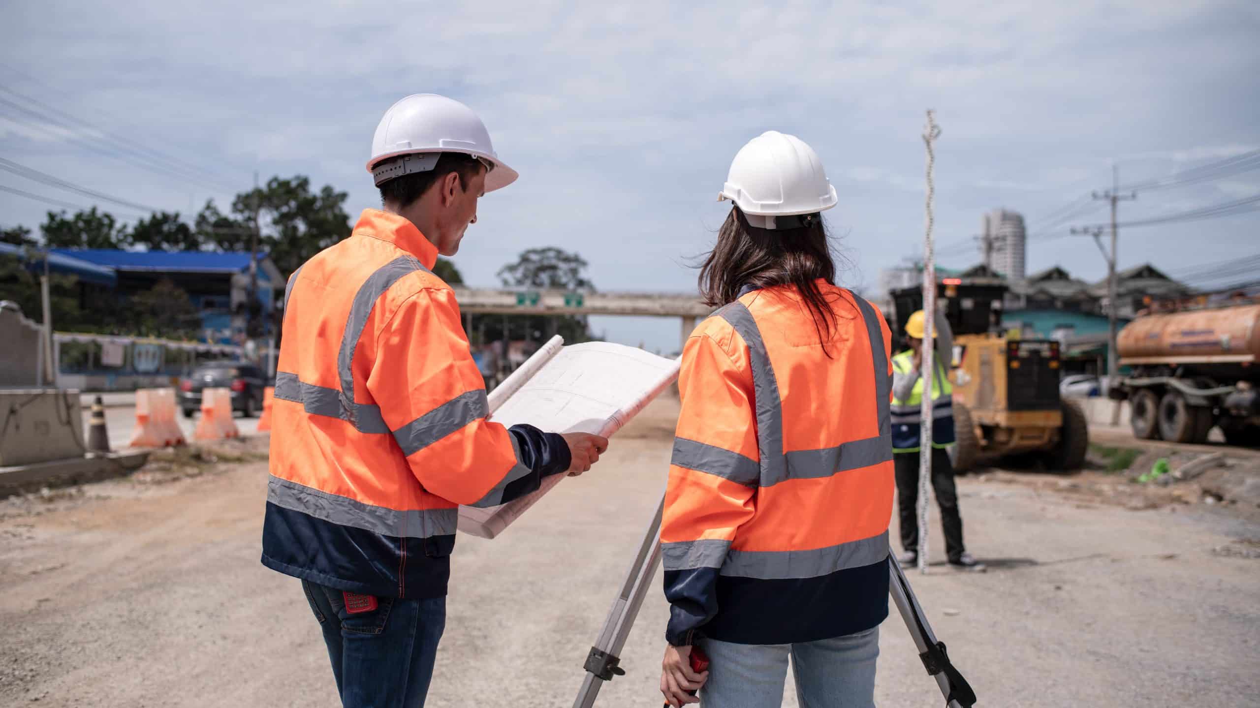 a man and woman in orange jackets and helmets looking at a blueprint